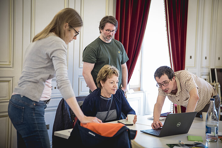 Un groupe de trois personnes de la Bibliothèque d’Yverdon-les-Bains participent à la formation à la chaîne de l’accessibilité du projet pilote Yverdon culture accessible. Les personnes montrent le site internet de la Bibliothèque sur un ordinateur à Monique Richoz qui est membre de la commission consultative d’Yverdon culture accessible et ancienne directrice de Pro Infirmis Vaud. 